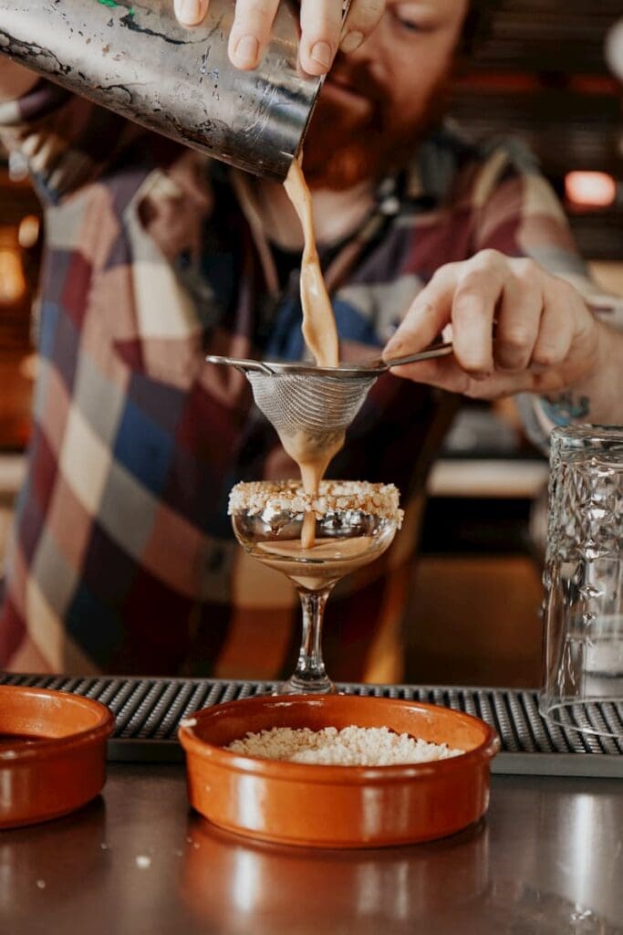 Jake pours a cocktail into a glass.