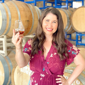 Image of Miranda in a rickhouse in front of barrels of bourbon